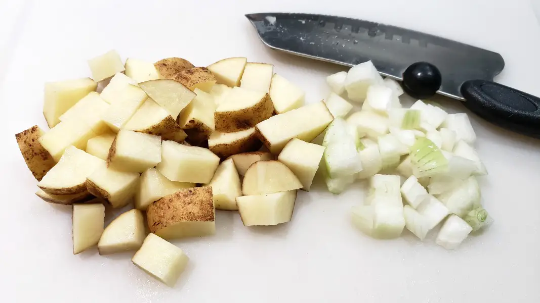 cubed potatoes and diced onion with a knife on a cutting board