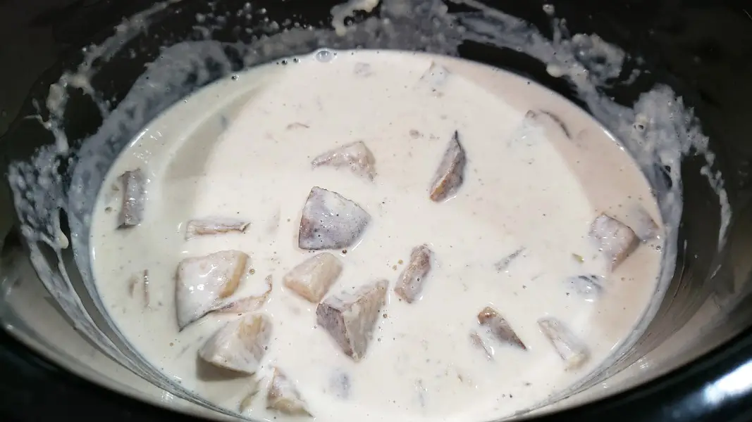 cream cheese, cheddar cheese and cream added to potato soup cooking in a slow cooker
