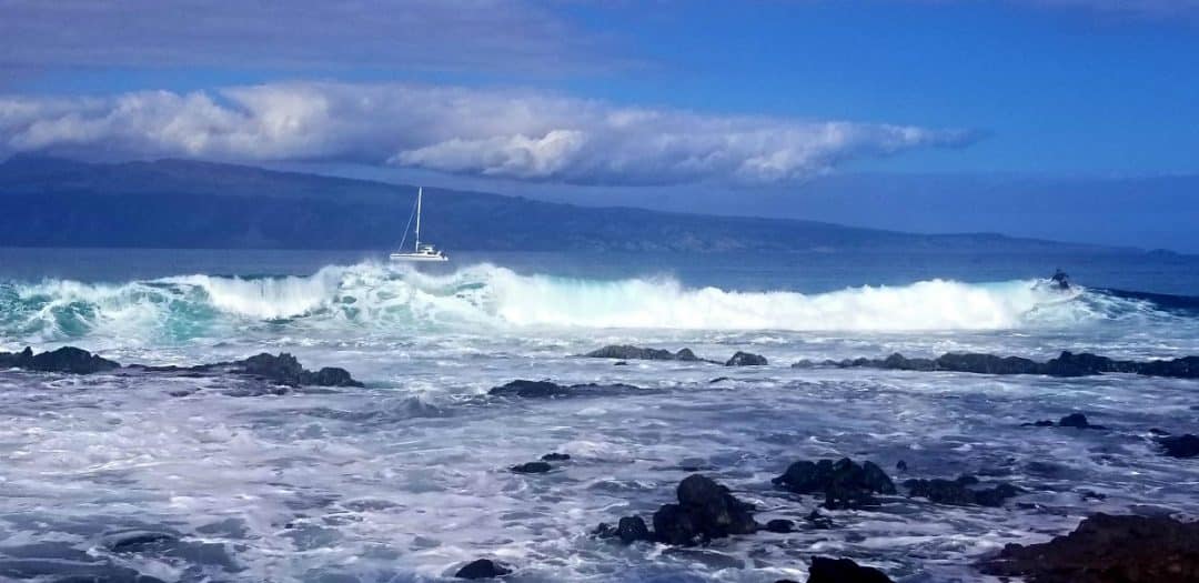 a sailboat beyond a huge wave on the ocean