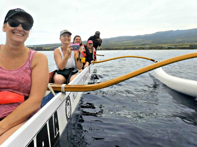 4 women and a man in an outrigger canoe on the ocean