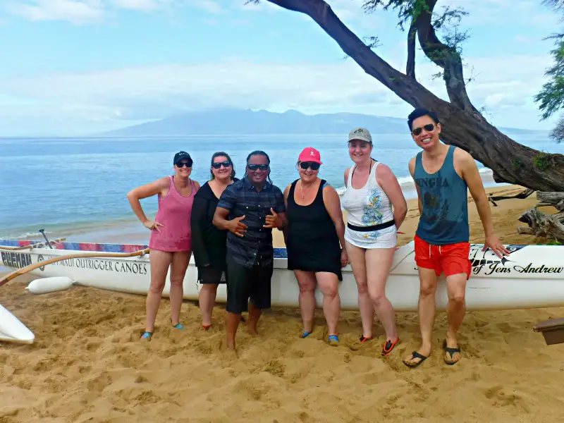 4 women and two men posing near an outrigger canoe on the beach
