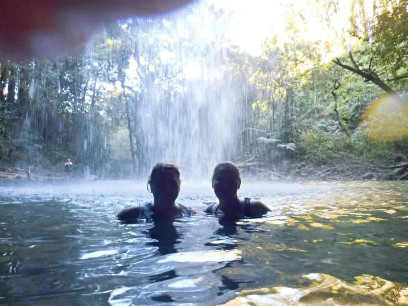 two women swimming under a waterfall