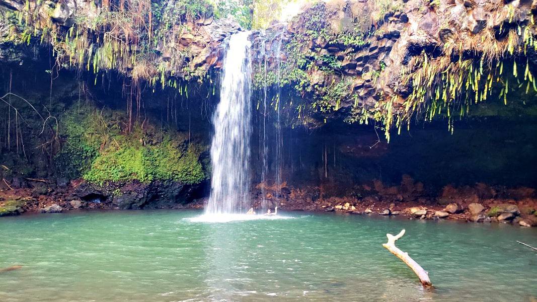 a waterfall flowing into a small lake with two women at the bottom of the waterfall