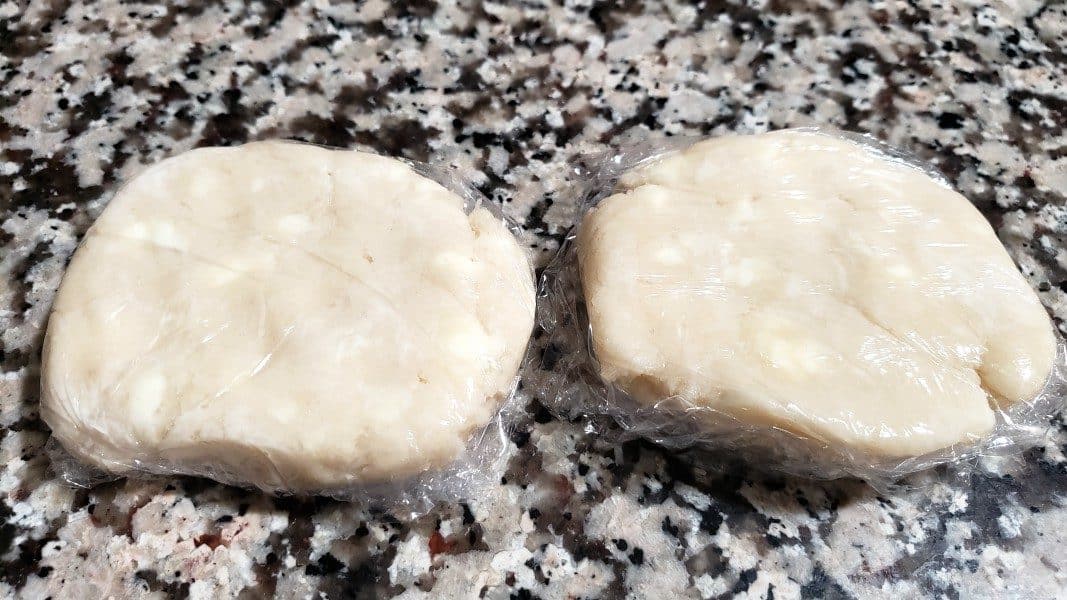 two pie dough discs wrapped with plastic wrap