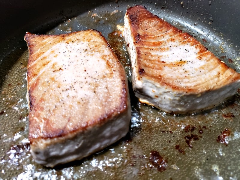 two tuna steaks searing in a pan