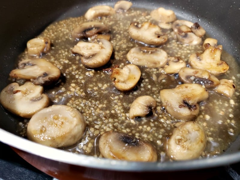 mushrooms, chicken stock, and garlic cooking in a pan