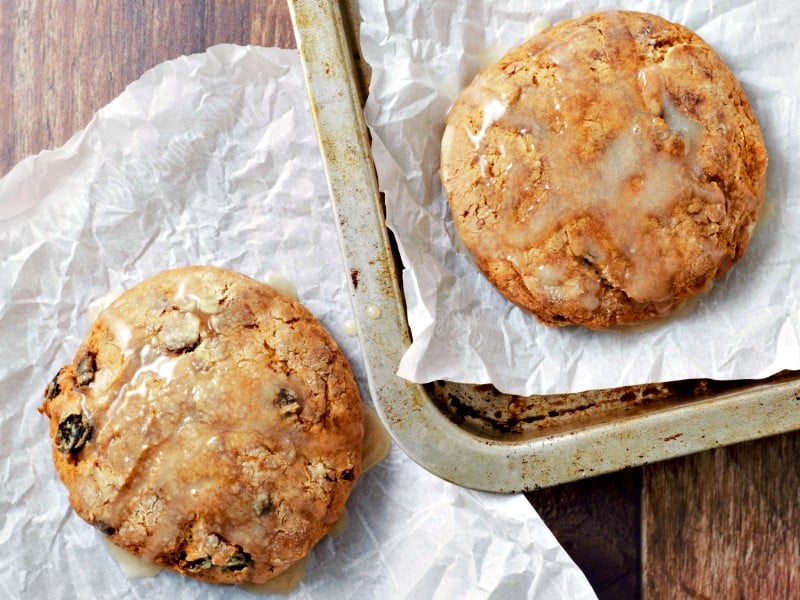 two Glazed Cinnamon Raisin Biscuits, one on a tray, one on parchment paper