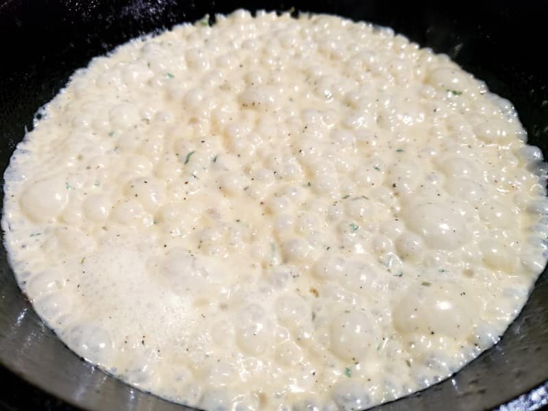 creamy parmesan sauce cooking in a cast iron skillet