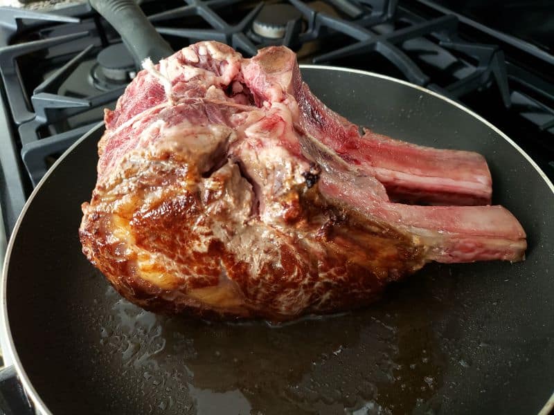 a standing prime rib roast searing in a frying pan