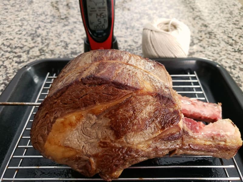 a standing prime rib roast on a roasting rack with a meat thermometer inserted
