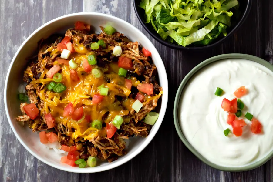 a Mexican Chicken Taco Bowl with sides of sour cream, and lettuce