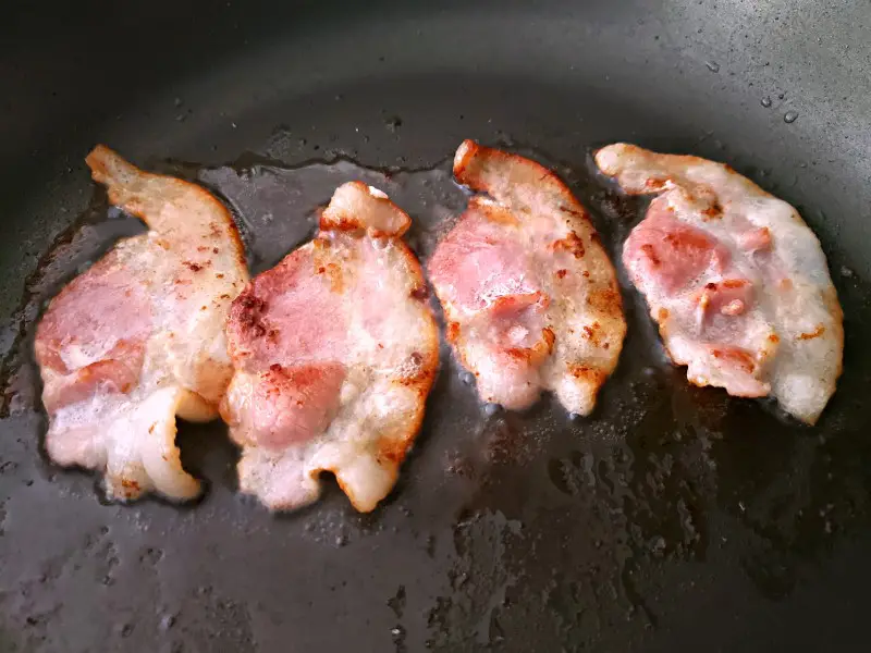 4 half pieces of bacon frying in a pan