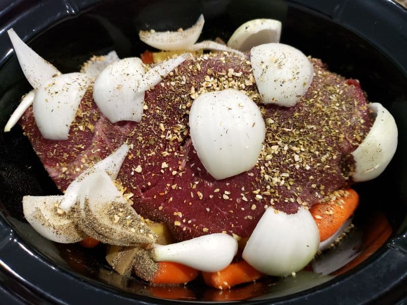 beef roast, onions, seasonings, carrots, and potatoes in a crockpot slow cooker
