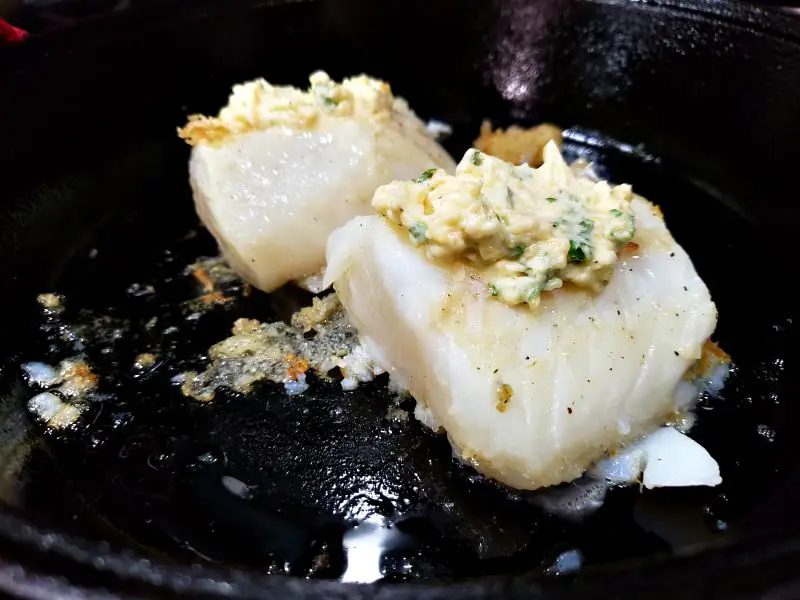 2 cod fillets in a cast iron skillet topped with garlic butter