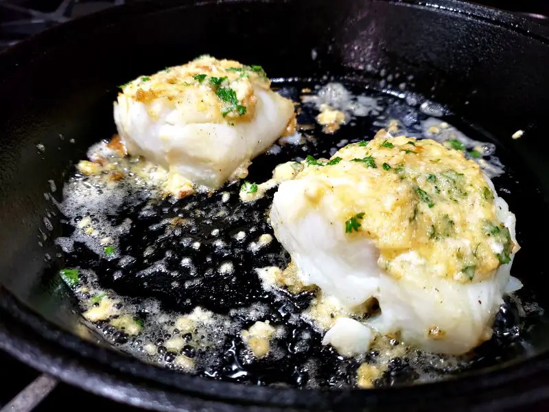 two oven roasted cod fillets in a cast iron skillet with garlic butter
