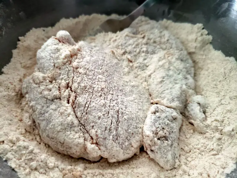 chicken thigh getting coated in flour and seasoning mixture