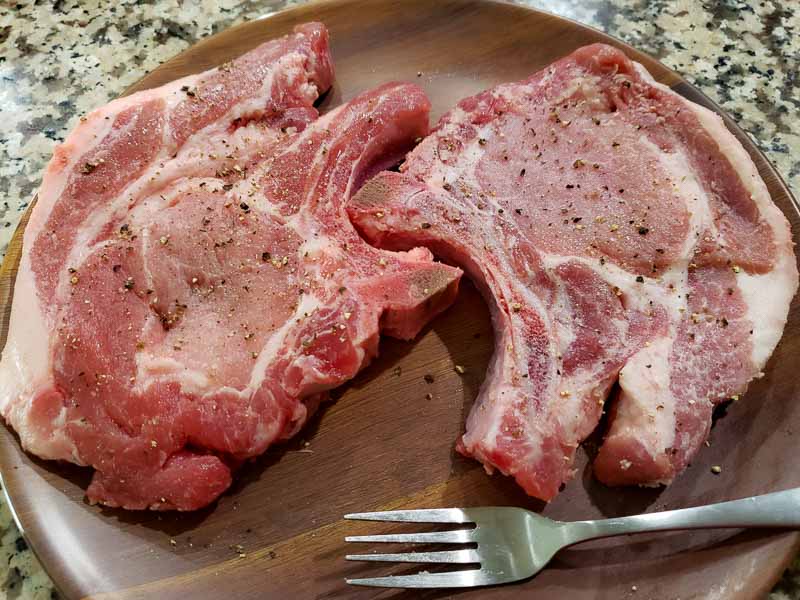 two chops on a plate seasoned with salt and pepper.