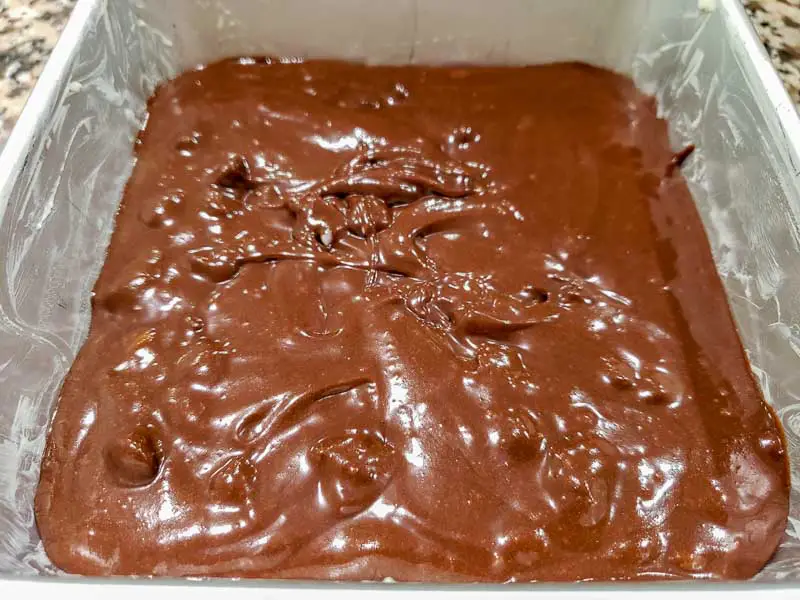 brownie batter in a buttered cake pan