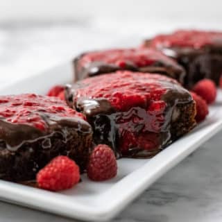 4 brownies with raspberry sauce and chocolate ganache on a platter.