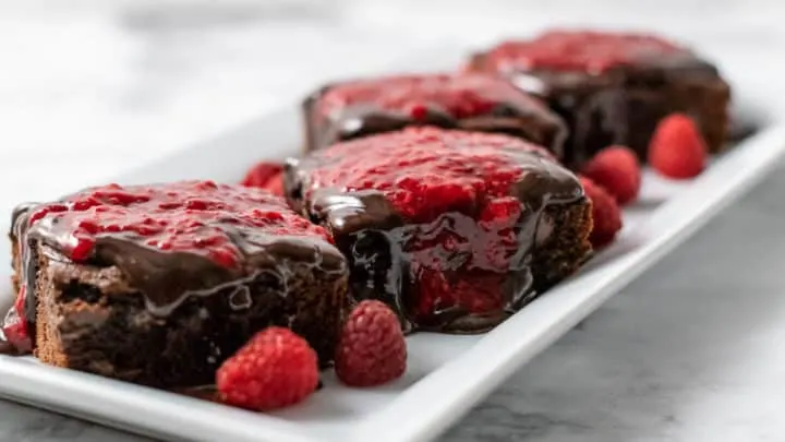 4 brownies with raspberry sauce and chocolate ganache on a platter