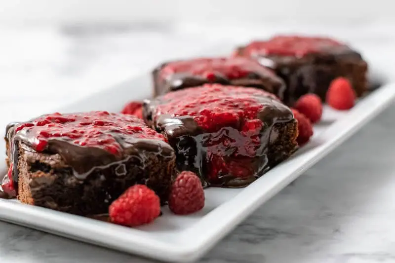 4 brownies with raspberry sauce and chocolate drizzle on a platter