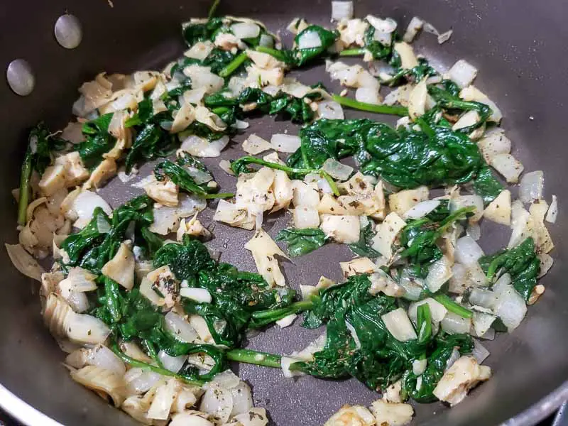 spinach artichoke mixture cooking in a pan.