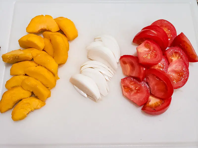 peaches, onions, and tomato wedges on a cutting board.