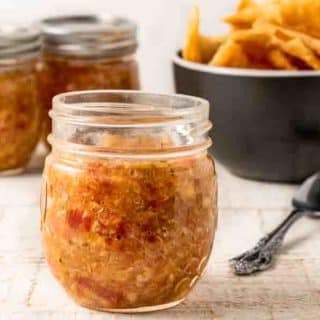 3 jars of tomato peach salsa and a bowl of tortilla chips.