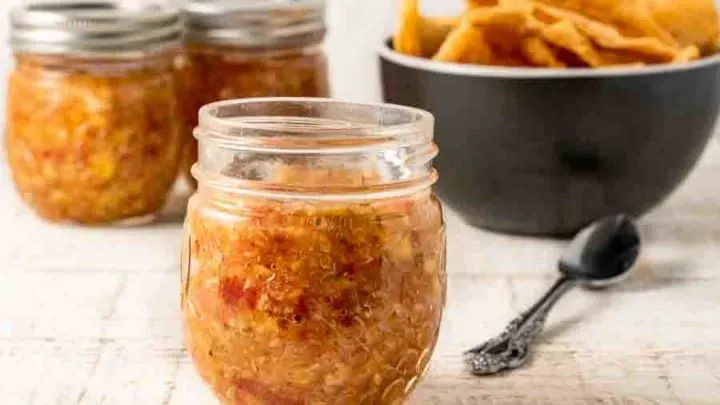 3 jars of tomato peach salsa and a bowl of tortilla chips.