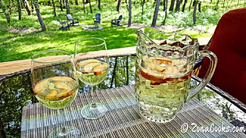 two glasses and a pitcher of white peach sangria.