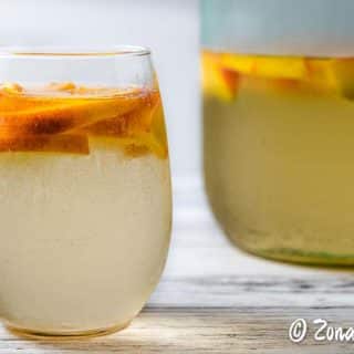 a glass and a pitcher of white peach sangria.