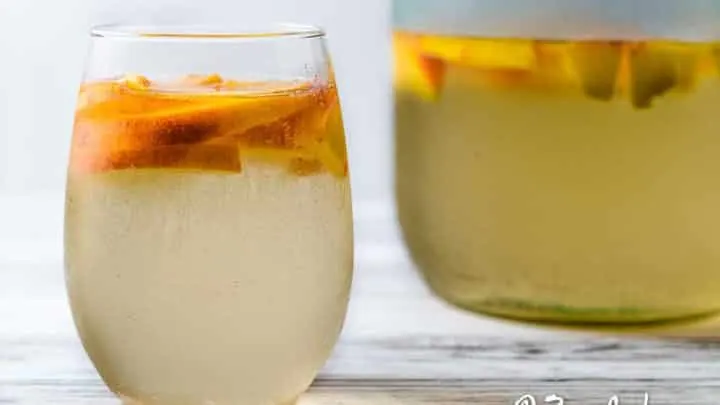 a glass and a pitcher of white peach sangria.