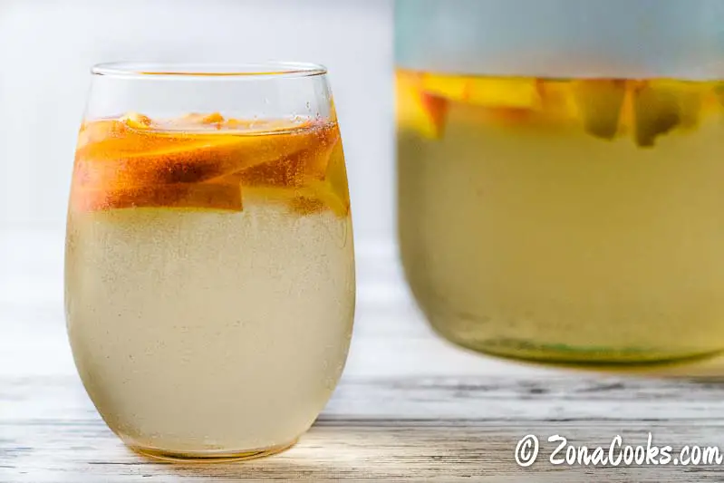 a glass and a pitcher of white peach sangria.