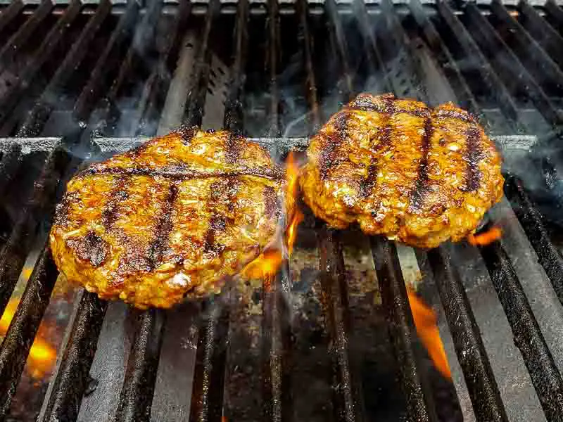 two hamburgers cooking on a grill