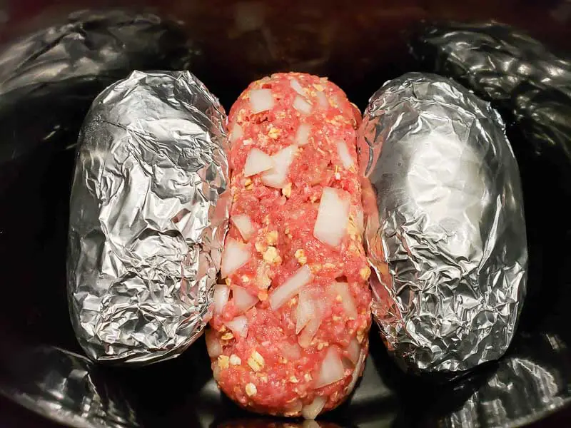easy meatloaf and two tin foil wrapped baked potatoes in a slow cooker crock pot.