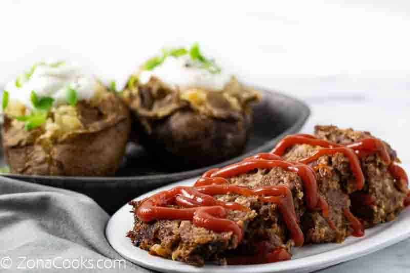 easy slow cooker meatloaf on a plate with baked potatoes on a tray that were made in a crock pot.
