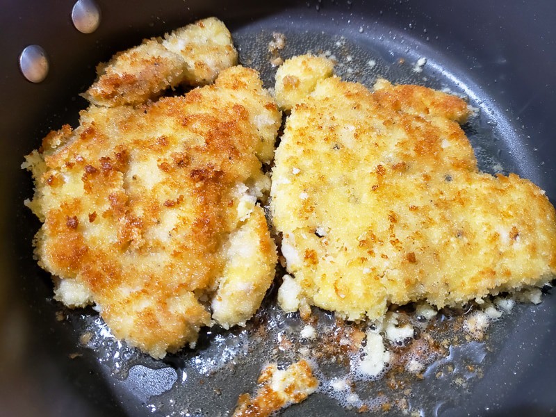 two pieces of crispy breaded chicken frying in a pan
