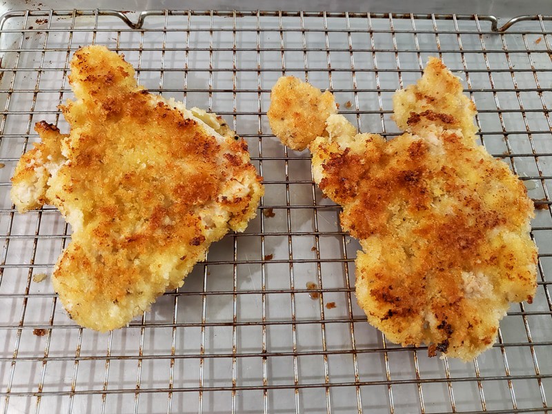 two pieces of crispy breaded chicken draining on a wire rack