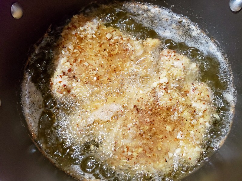 two almond and panko crusted chicken breasts frying in oil.