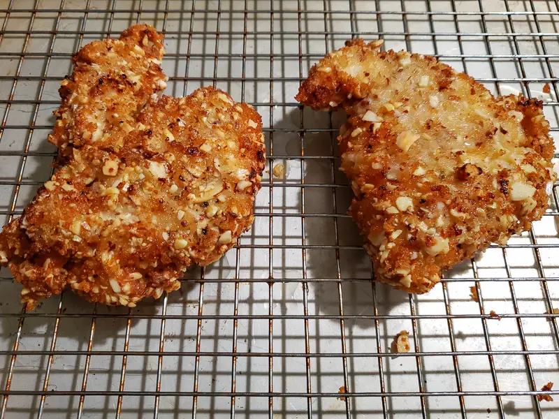 two cooked almond crusted chicken breasts draining on a rack.