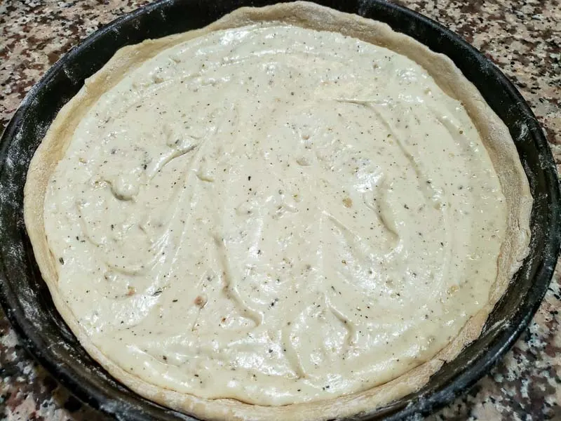 white garlic sauce spread over pizza dough