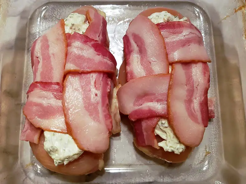 bacon weaves placed on top of the chicken and cream cheese in a dish.