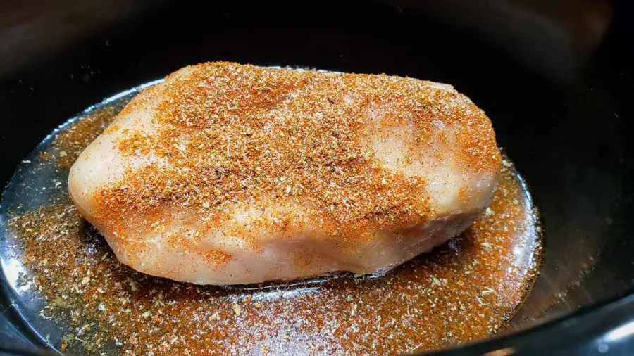 a boneless chicken cutlet in a crockpot sprinkled with taco seasoning.