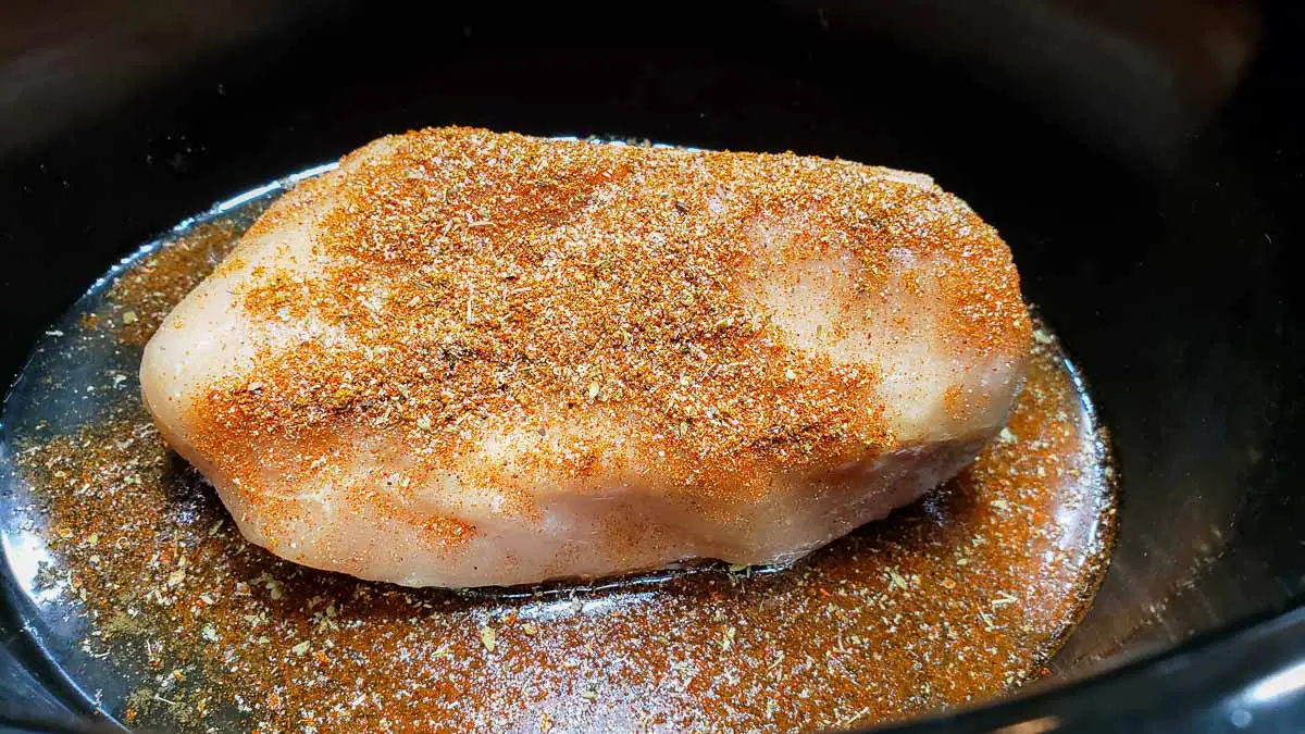a boneless chicken cutlet in a slow cooker crock pot sprinkled with taco seasoning.