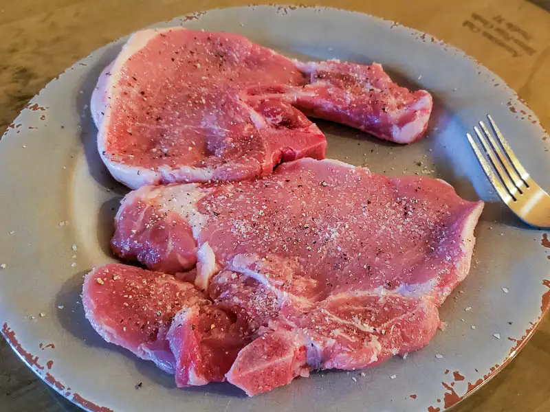 two pork chops sprinkled with salt and pepper.