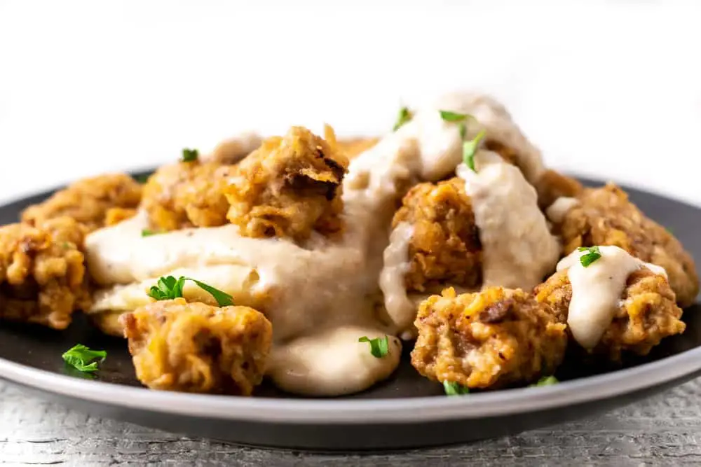 Chicken Fried Steak Bites and White Country Gravy over Homemade Buttermilk Biscuits on a plate.