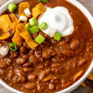 a bowl of chili topped with sour cream, green onion, and fritos.
