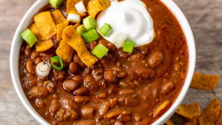 a bowl of chili topped with sour cream, green onion, and fritos