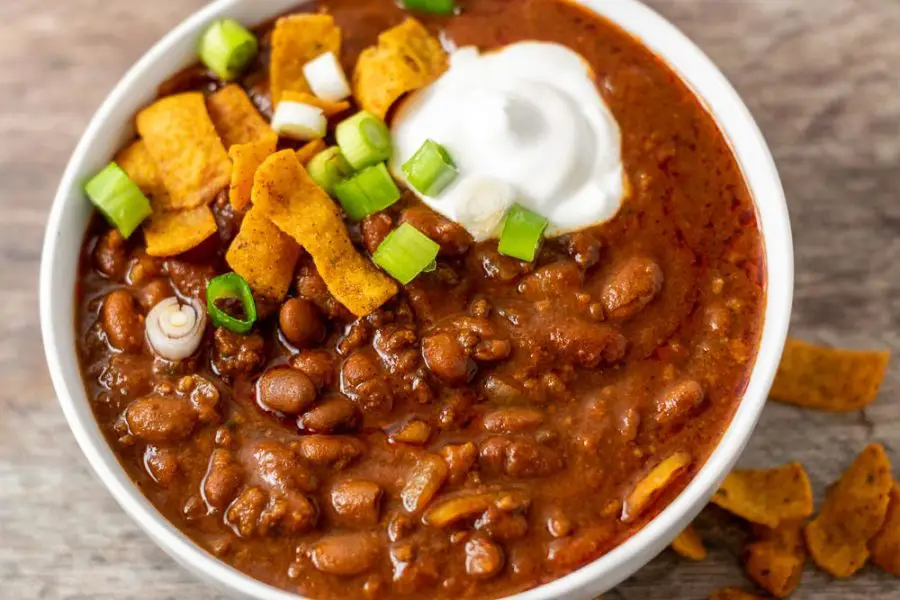 a bowl of chili topped with sour cream, green onion, and fritos.