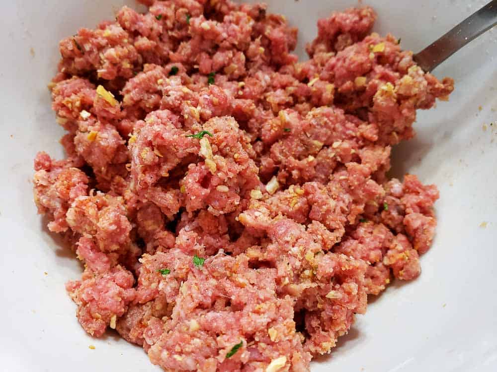 ground beef, onion flakes, onion powder, parsley, celery seed, paprika, black pepper, bread crumbs, and milk mixed together in a bowl.